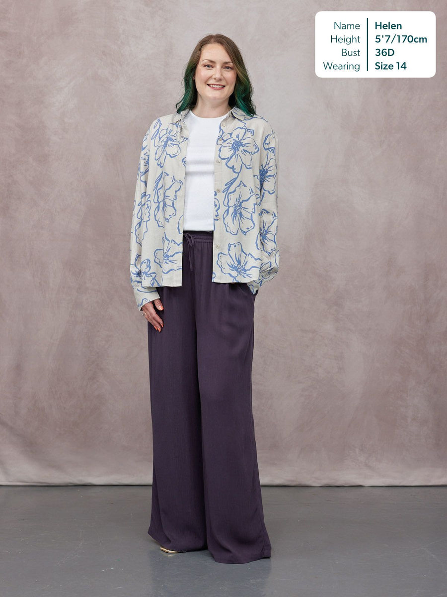 Model wearing wide-leg dark purple trousers with a drawstring waist, styled with an open blue floral shirt and white tee.