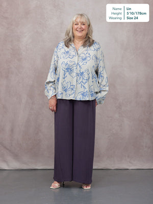 Model wearing wide-leg dark purple trousers with a loose blue floral print shirt, styled with strappy heels.