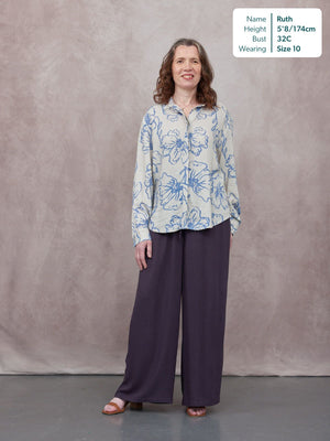 Model wearing wide-leg dark purple trousers with a blue floral print shirt, styled with tan mule sandals.