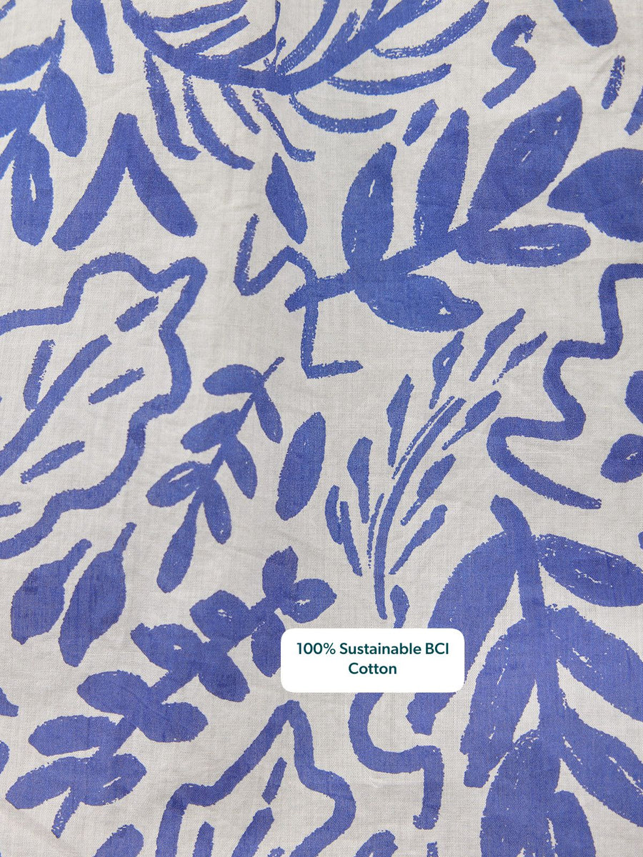 Close-up of white cotton fabric with a bold blue abstract botanical print featuring leaves and organic brushstroke shapes.