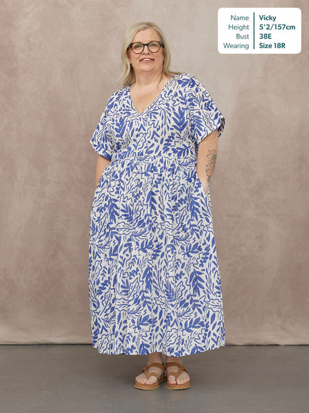 Model wearing a white midi dress with blue botanical print, V-neck, short sleeves, and elasticated waist, styled with tan…