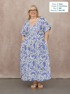 Model wearing a white midi dress with blue botanical print, V-neck, short sleeves, and elasticated waist, styled with tan…
