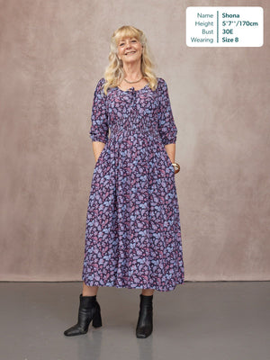 Model wearing a navy floral midi dress with shirred waist, three-quarter sleeves, and tie neckline, styled with boots