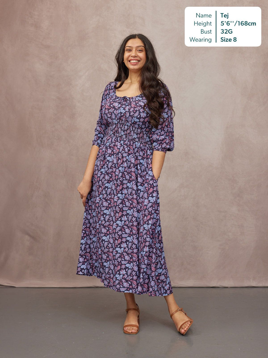 Model wearing a navy floral midi dress with square neckline, shirred waist, puff sleeves, and tan sandals