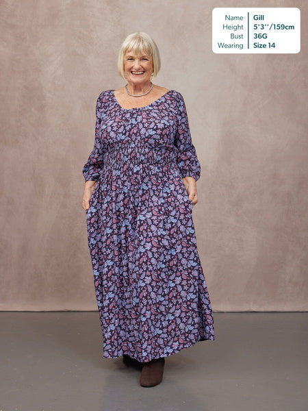Model wearing a navy floral maxi dress with a scoop neck, shirred waist, long sleeves, and full skirt