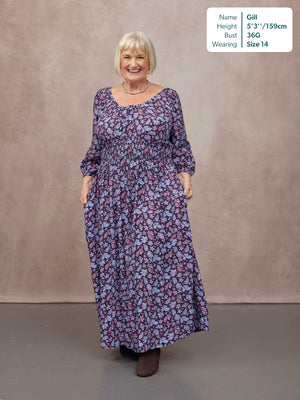 Model wearing a navy floral maxi dress with a scoop neck, shirred waist, long sleeves, and full skirt