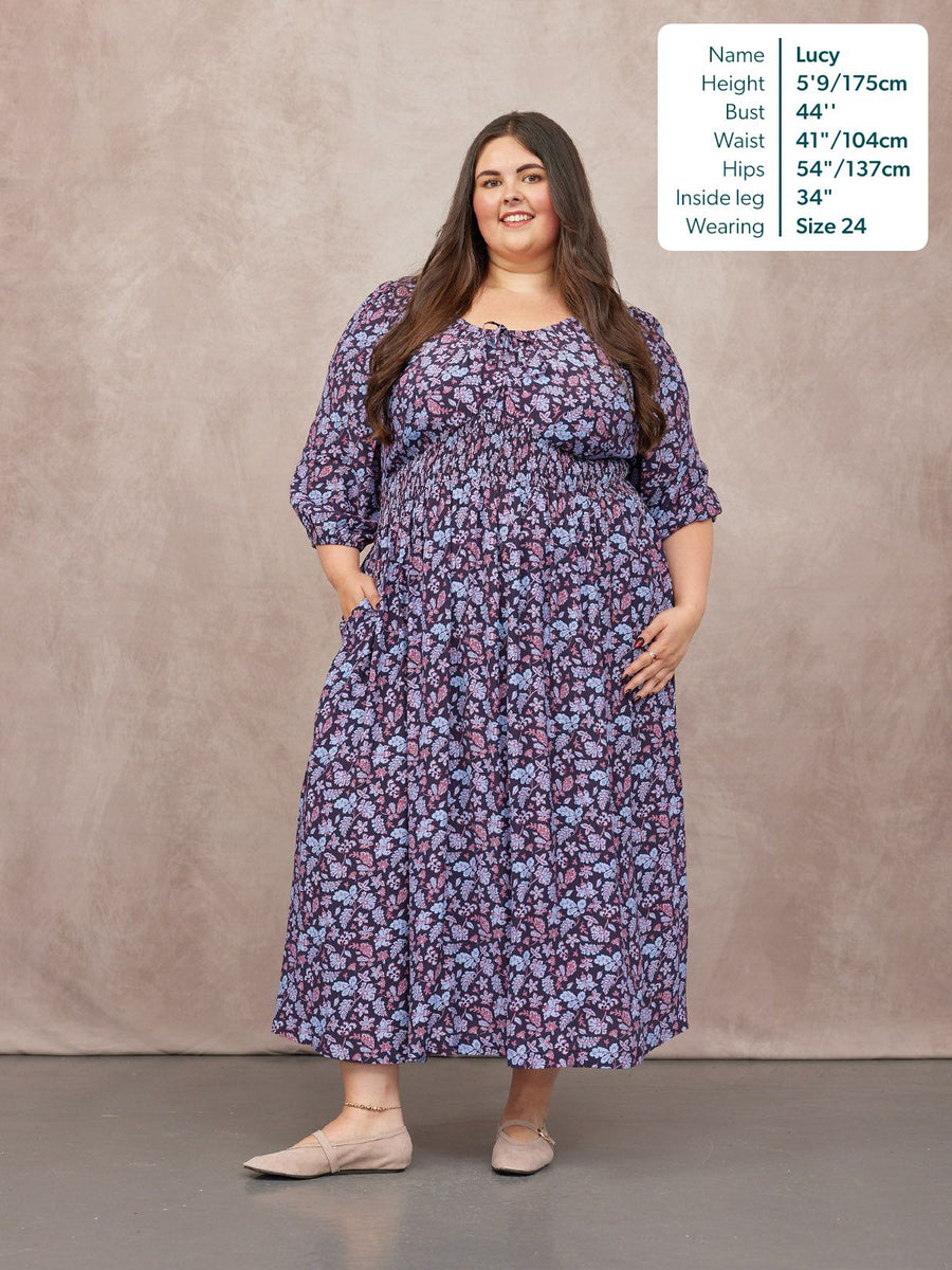 Model wears a navy floral maxi dress with a smocked waist, tie neckline, 3/4 sleeves, and side pockets