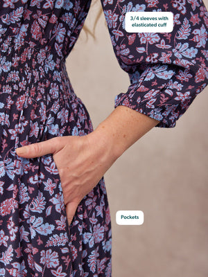 Close-up of a navy floral dress on a model, showing smocked waist, 3/4 elasticated cuffs, and hand in side pocket.