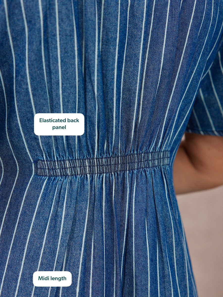 Close-up of a blue pinstripe denim midi dress showing an elasticated back waist panel with gathered fabric detail.
