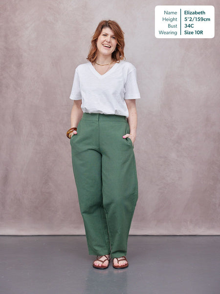 Myrtle Barrel Leg Trouser in green, worn with white v-neck tee and sandals, model smiling, hands in pockets