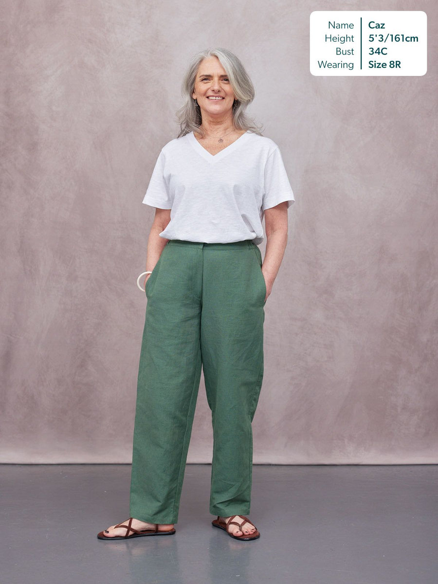 Myrtle Barrel Leg Trouser in green linen, worn by a smiling woman with white V-neck tee and brown sandals, studio backdrop