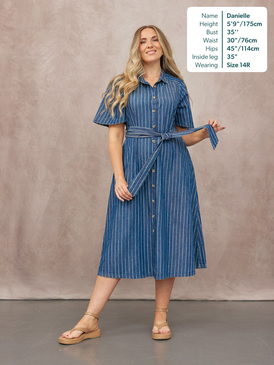 Model wearing a blue denim pinstripe midi shirt dress with short flutter sleeves, button front, and tied waist belt, styled…