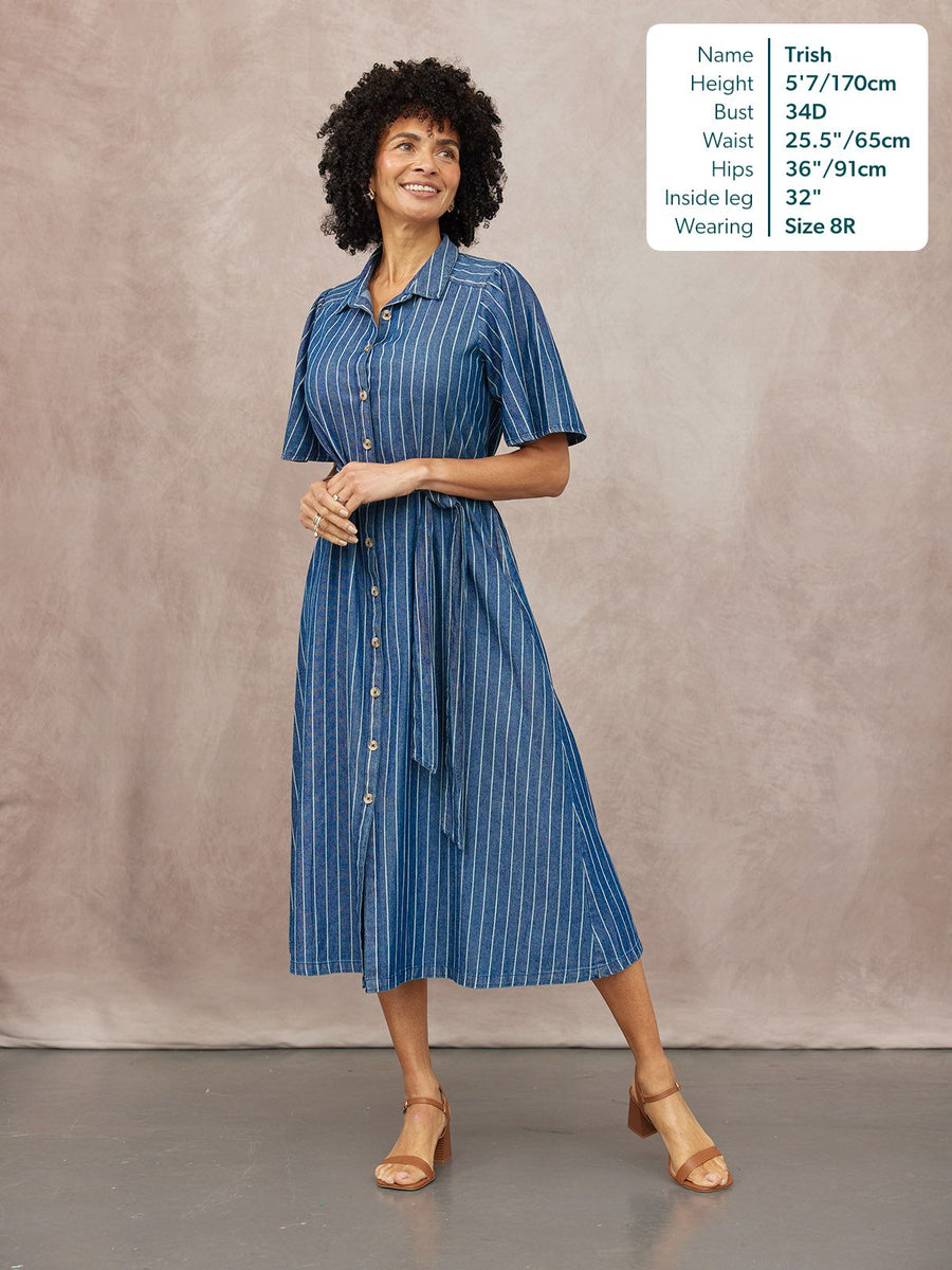 Model wearing a blue denim stripe midi shirt dress with short sleeves, button front, and tie waist, styled with tan…