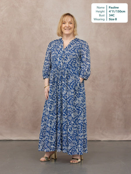 Model wearing a blue paisley print maxi dress with a V-neck, three-quarter sleeves, and tiered skirt, styled with gold…