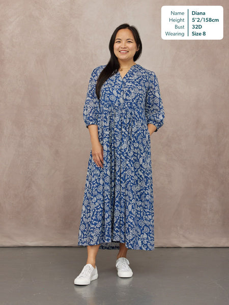 Model wears a blue and white paisley print midi dress with V-neck, puff sleeves, and tiered skirt, styled with white…
