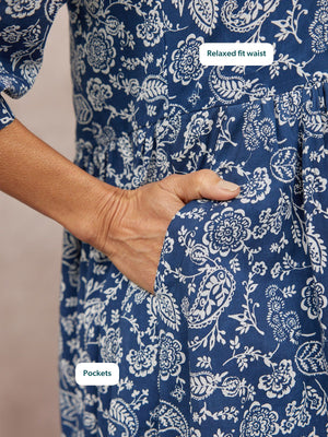 Close-up of a model's hand tucked into the side pocket of a navy blue floral print dress with a relaxed fit waist.