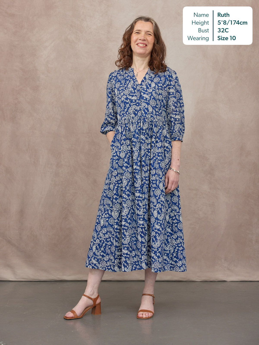 Model wearing a blue and white paisley print midi dress with V-neck, 3/4 sleeves, and tiered skirt, styled with tan heeled…