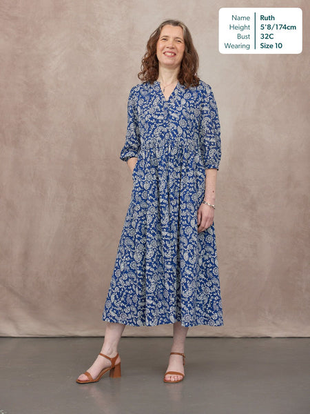 Model wearing a blue and white paisley print midi dress with V-neck, 3/4 sleeves, and tiered skirt, styled with tan heeled…