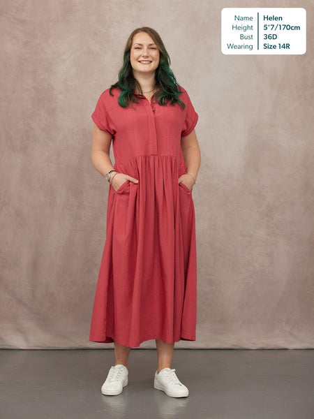 Model wearing a raspberry red midi shirt dress with short sleeves, gathered skirt, and side pockets, styled with white…