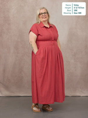 Model wearing a terracotta short-sleeve shirt-neck midi dress with a gathered skirt and side pockets, styled with tan…