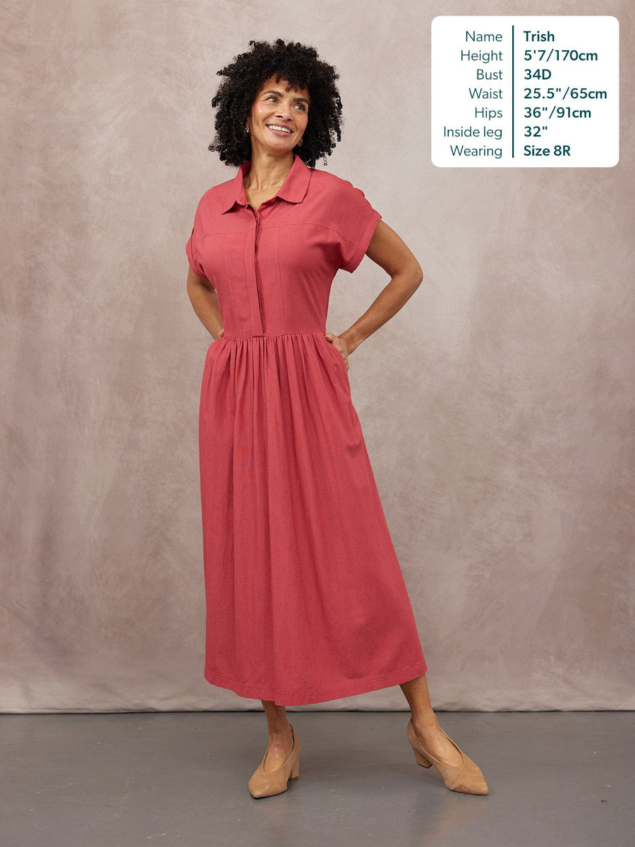 Model wears a coral pink midi shirt dress with a full gathered skirt, short sleeves, collar, and zip front, styled with…