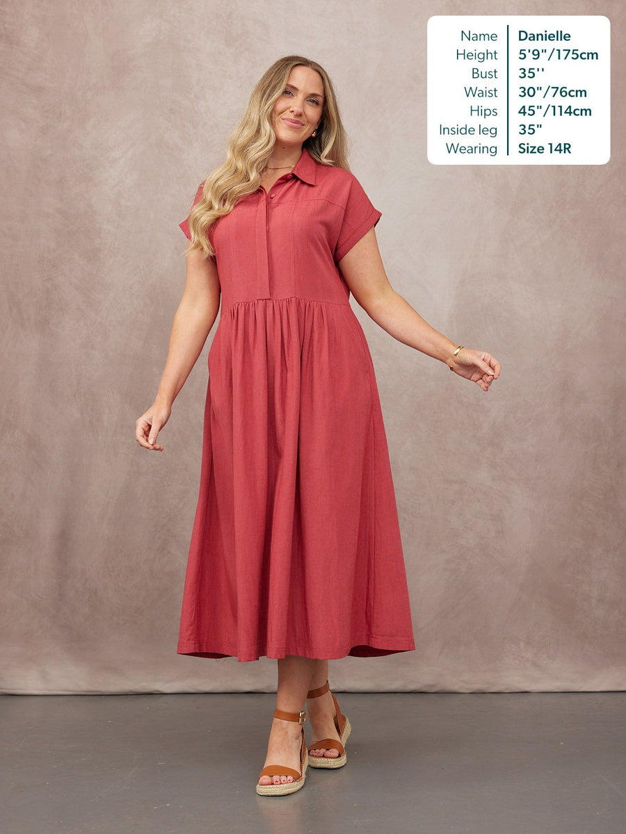 Model wears a coral red short-sleeve shirt midi dress with a gathered skirt, paired with tan wedge sandals.