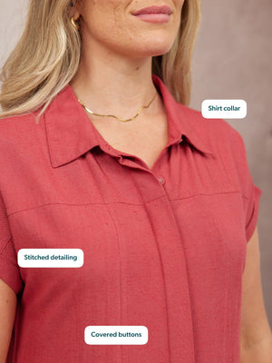 Close-up of a model wearing a rose-red sleeveless shirt with a shirt collar, covered buttons, and stitched detailing.