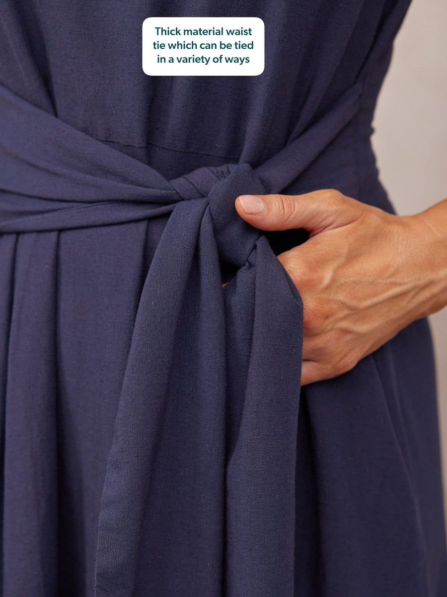Close-up of a navy blue dress with a thick fabric waist tie being knotted by a model's hand.