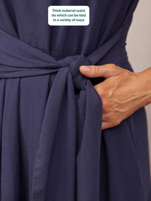 Close-up of a navy blue dress with a thick fabric waist tie being knotted by a model's hand.