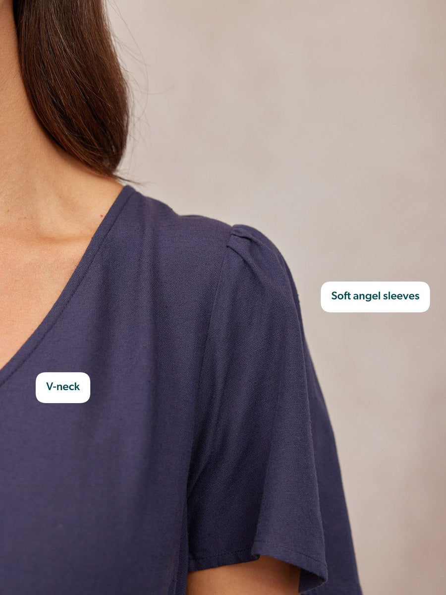 Close-up of a model wearing a navy blue v-neck top with soft angel sleeves against a grey background.