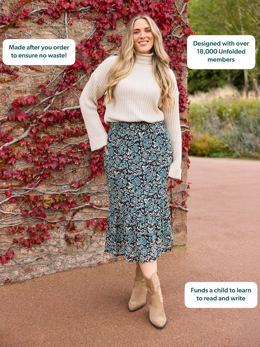 Model wearing a navy floral midi skirt with a cream ribbed turtleneck jumper and tan ankle boots, standing outdoors.