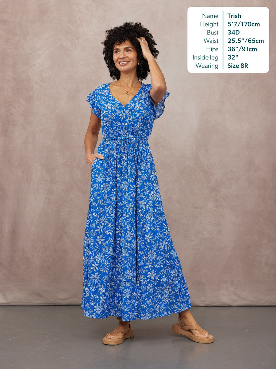 Model wearing a blue floral maxi dress with flutter sleeves, V-neck, and cinched waist, styled with tan sandals.