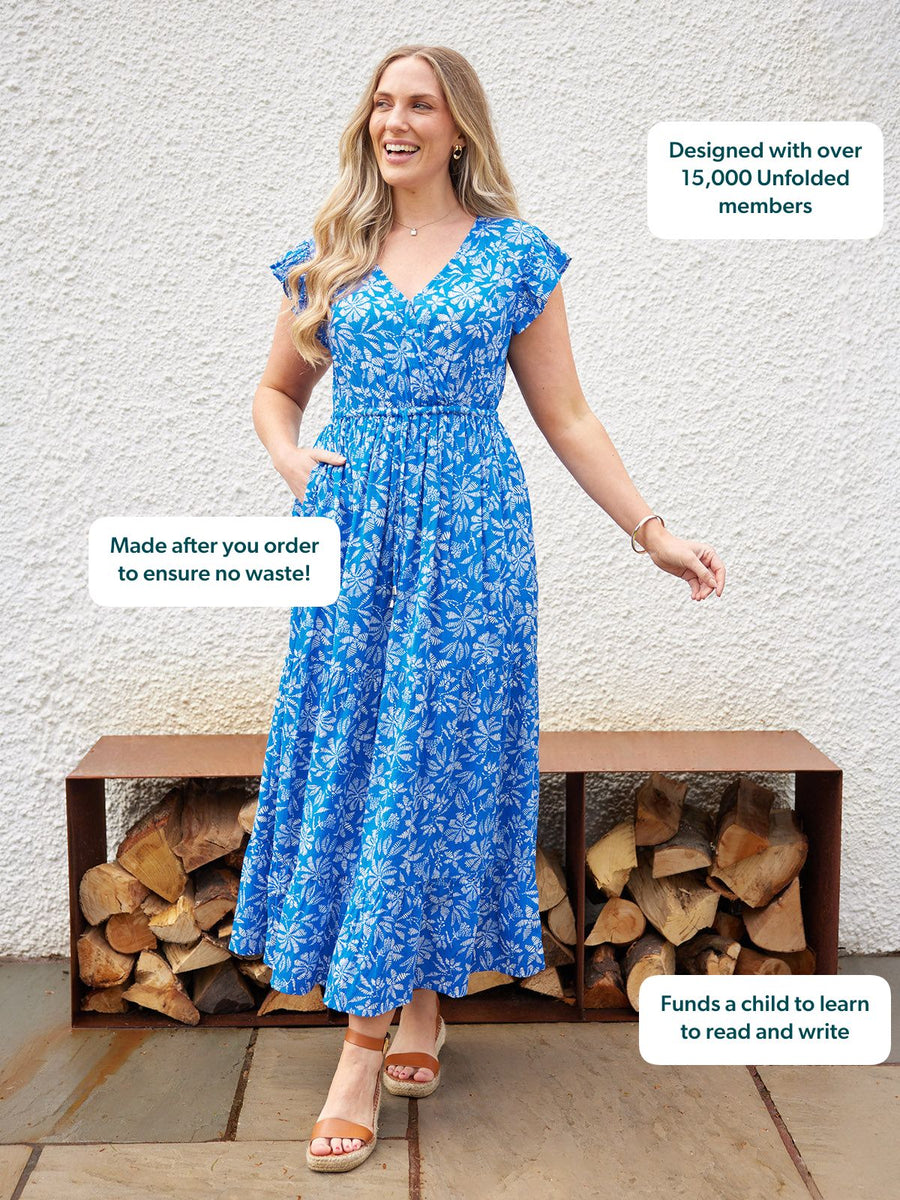 Model wearing a blue floral midi dress with flutter sleeves, V-neckline, and fitted waist, styled with tan wedge sandals…