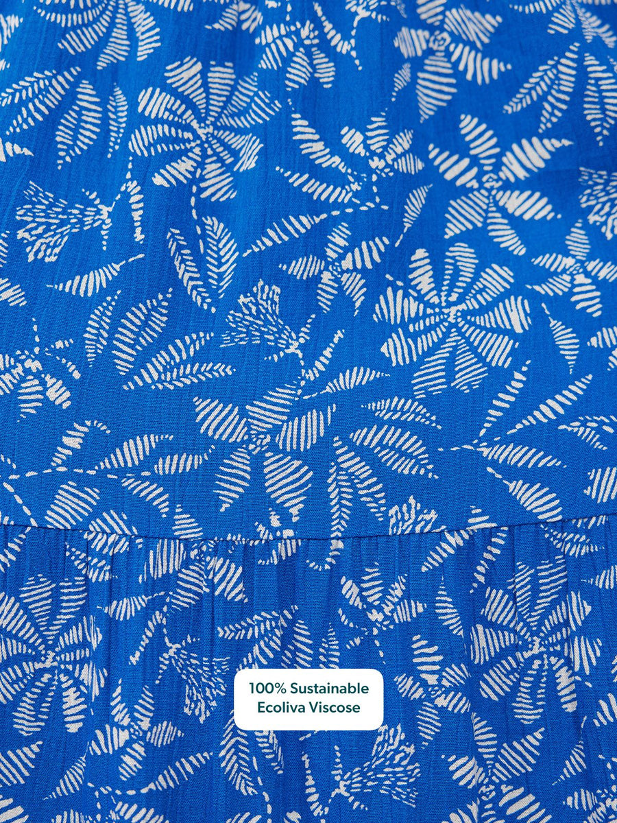Close-up of cobalt blue tiered dress fabric with white botanical leaf print and a gathered seam detail.