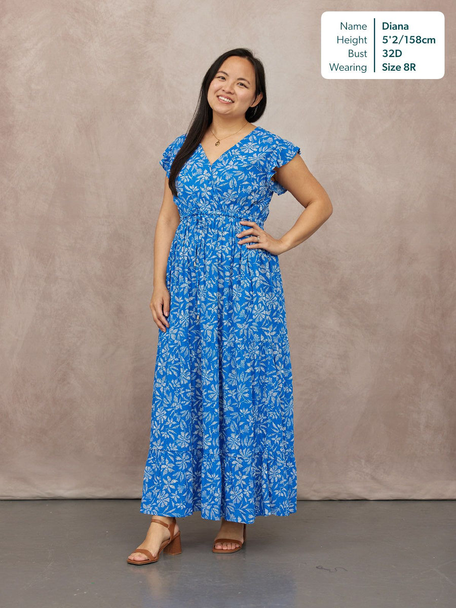 Model wearing a blue floral maxi dress with a V-neck, flutter sleeves, and smocked waist, paired with tan block-heel sandals.