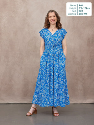 Model wearing a blue floral maxi dress with flutter sleeves, V-neckline, drawstring waist, and flared skirt, styled with…