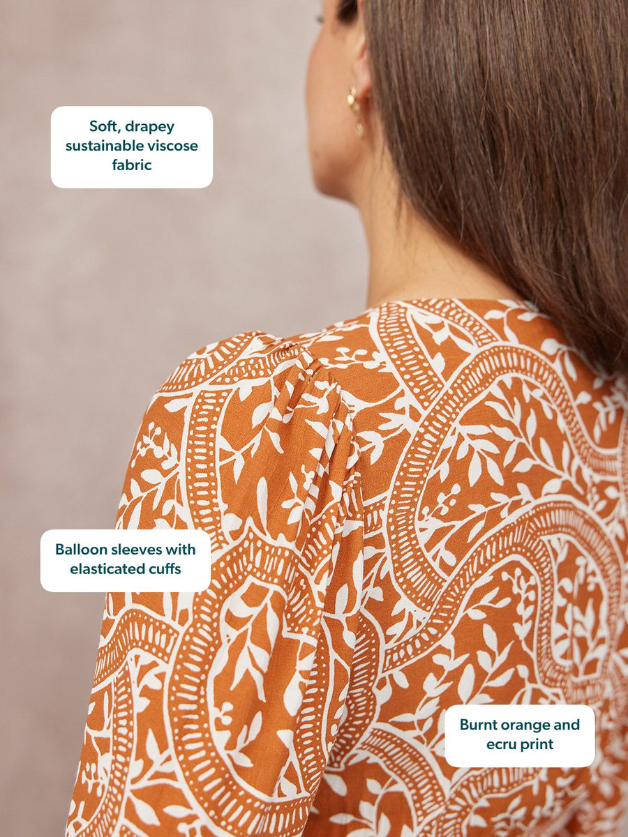 Close-up of a model's back wearing a burnt orange and ecru floral print top with balloon sleeves.