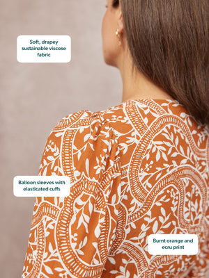 Close-up of a model's back wearing a burnt orange and ecru floral print top with balloon sleeves.