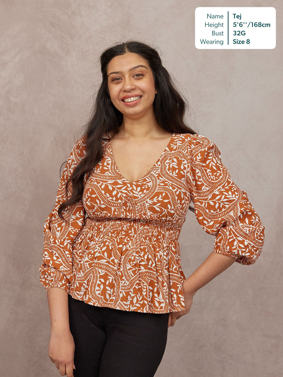 Model wearing a rust orange and white paisley print V-neck top with puff sleeves and a shirred waist