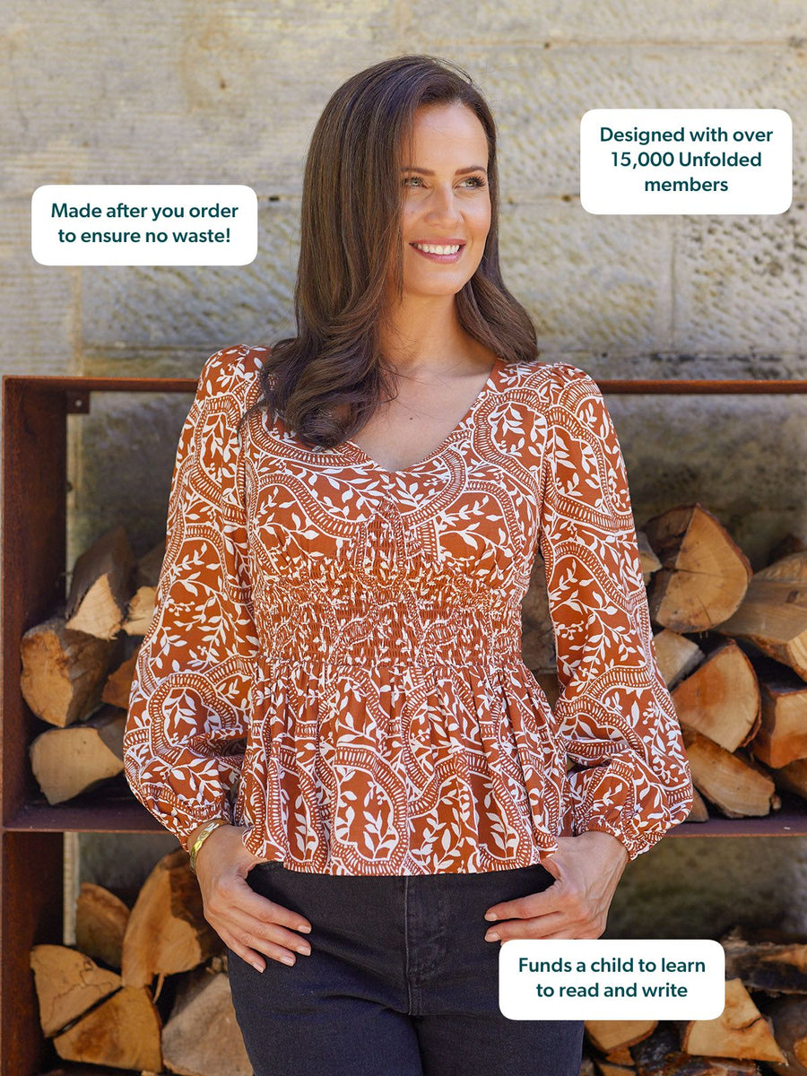 Model wearing a rust and white floral print smocked-waist peplum top with balloon sleeves and a V-neckline