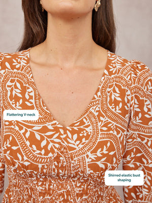 Close-up of a rust orange and white paisley print dress with a deep V-neck and shirred elastic waist, worn by a model.