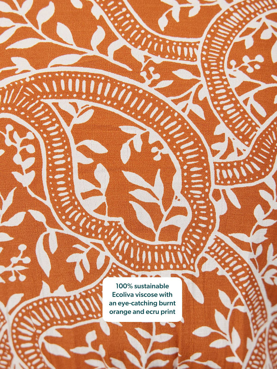 Close-up of burnt orange fabric with an ecru botanical leaf and vine print.