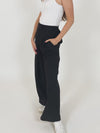 A video of a model wearing the Lana sustainable trousers and a white vest top. They are turning around to show the outfit in full, with a close up of the pockets and the zip and clasp fastening at the end. 