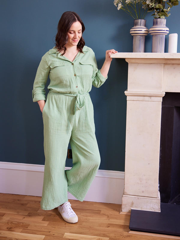 A model leans against a mantlepiece wearing the sustainable Clara jumpsuit from Unfolded. They are smiling and looking down. 