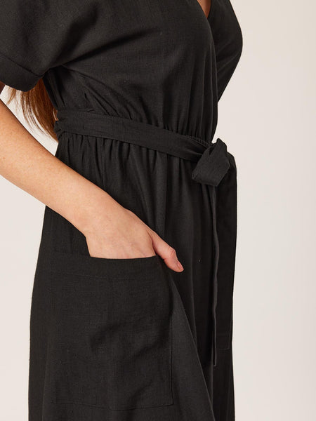 A close up of a model wearing the sustainable Daisy wrap dress in black, with a focus on the pocket. 