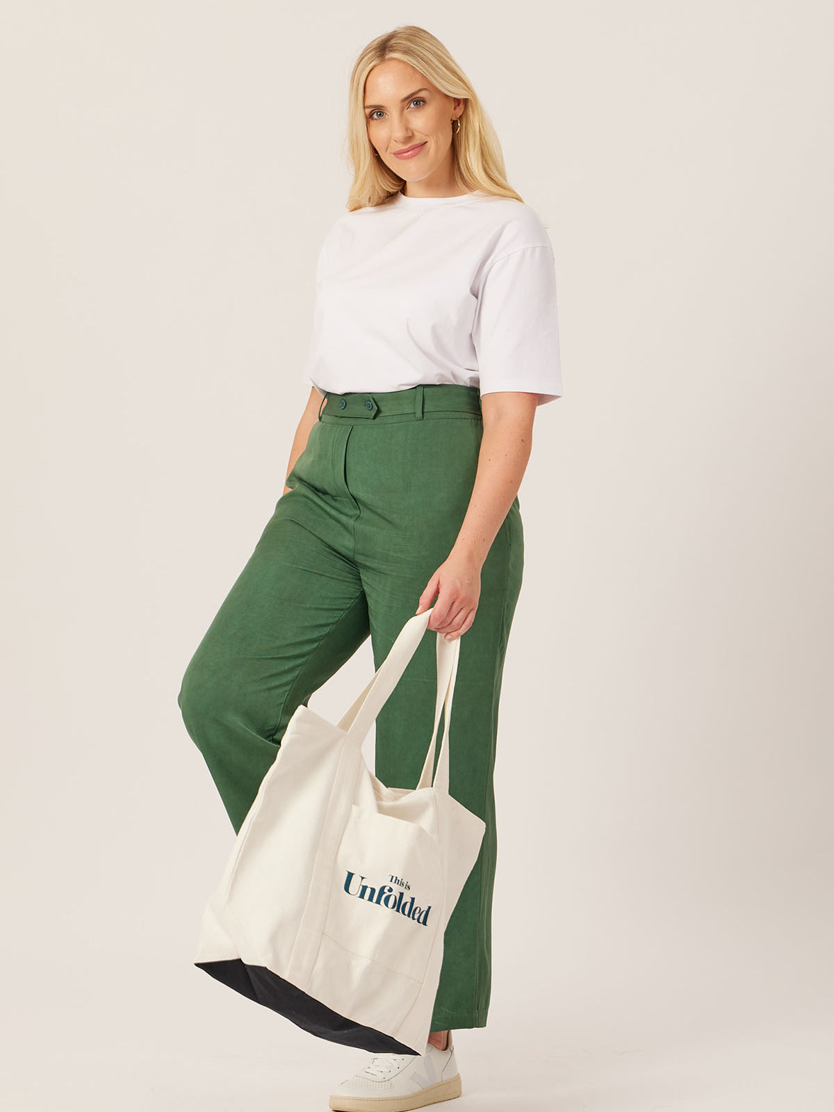 A model carries the Joey bag in their hand whilst wearing the white Penny t-shirt and olive Beth trousers, pictured against a white backdrop. 