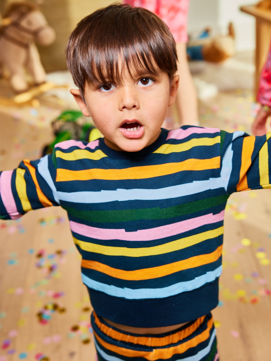 Child wearing sustainable kids tracksuit Elias with a wavy stripe motif on a navy base, looking at the camera, standing in a party environment