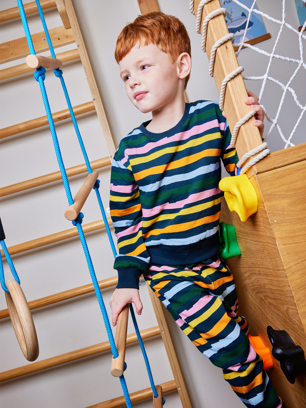 Child wearing the Elias sustainable kids tracksuit set in wavy multicolour stripe, pictured playing on an indoor climbing frame.