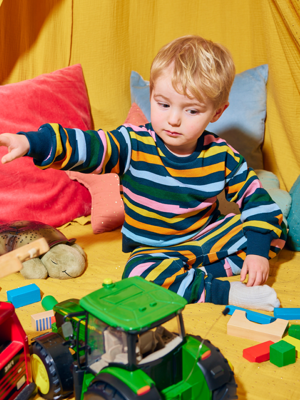 Child wearing the Elias sustainable kids tracksuit set in wavy multicolour stripe, pictured playing with bright toys.