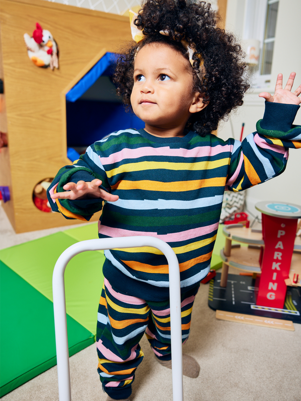 Child wearing the Elias eco-friendly kids tracksuit set in wavy multicolour stripe, pictured playing with toys.